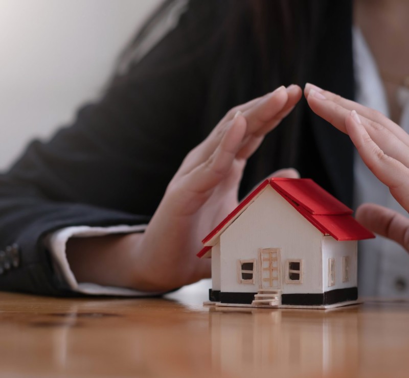Protect your house concept. Small toy house covered by hands.